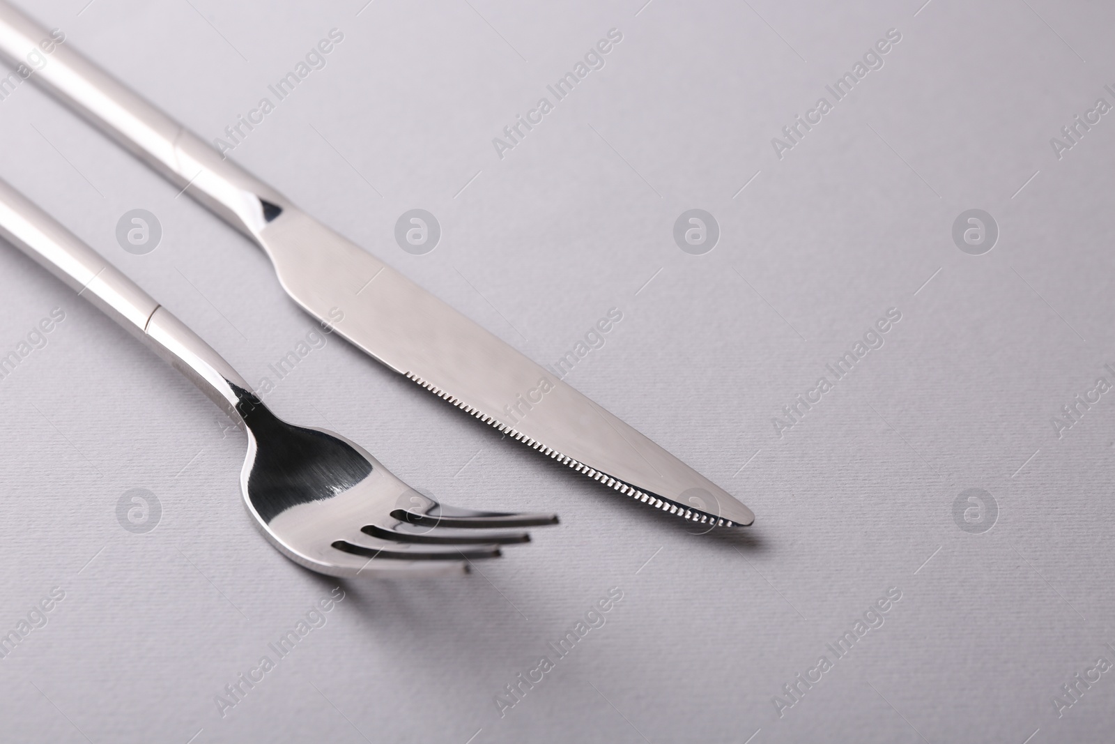 Photo of Stylish cutlery. Silver knife and fork on gray background, closeup. Space for text