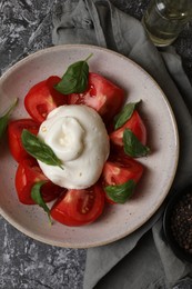 Photo of Delicious burrata cheese with tomatoes and basil, oil and peppercorns on grey table, flat lay
