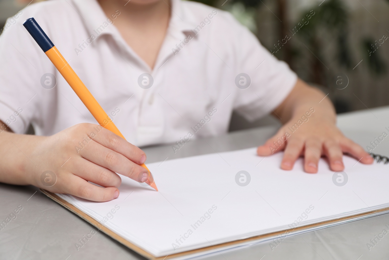 Photo of Little boy drawing with pencil at grey textured table indoors, closeup. Child`s art