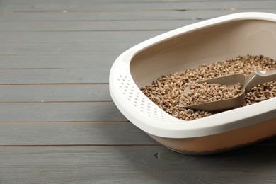 Photo of Cat litter tray with filler and scoop on grey wooden floor, closeup. Space for text