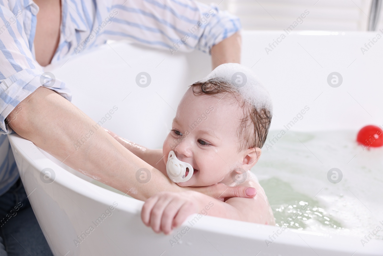 Photo of Mother bathing her cute little baby in tub at home