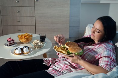 Photo of Happy overweight woman eating french fries with burgers at home