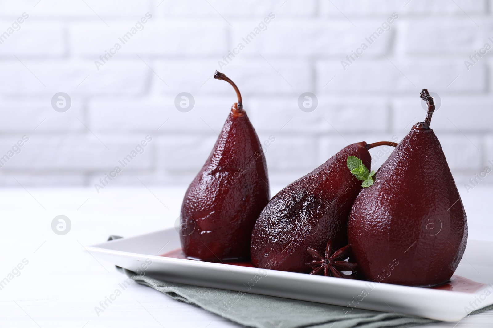 Photo of Tasty red wine poached pears with mint and anise on white wooden table, closeup. Space for text