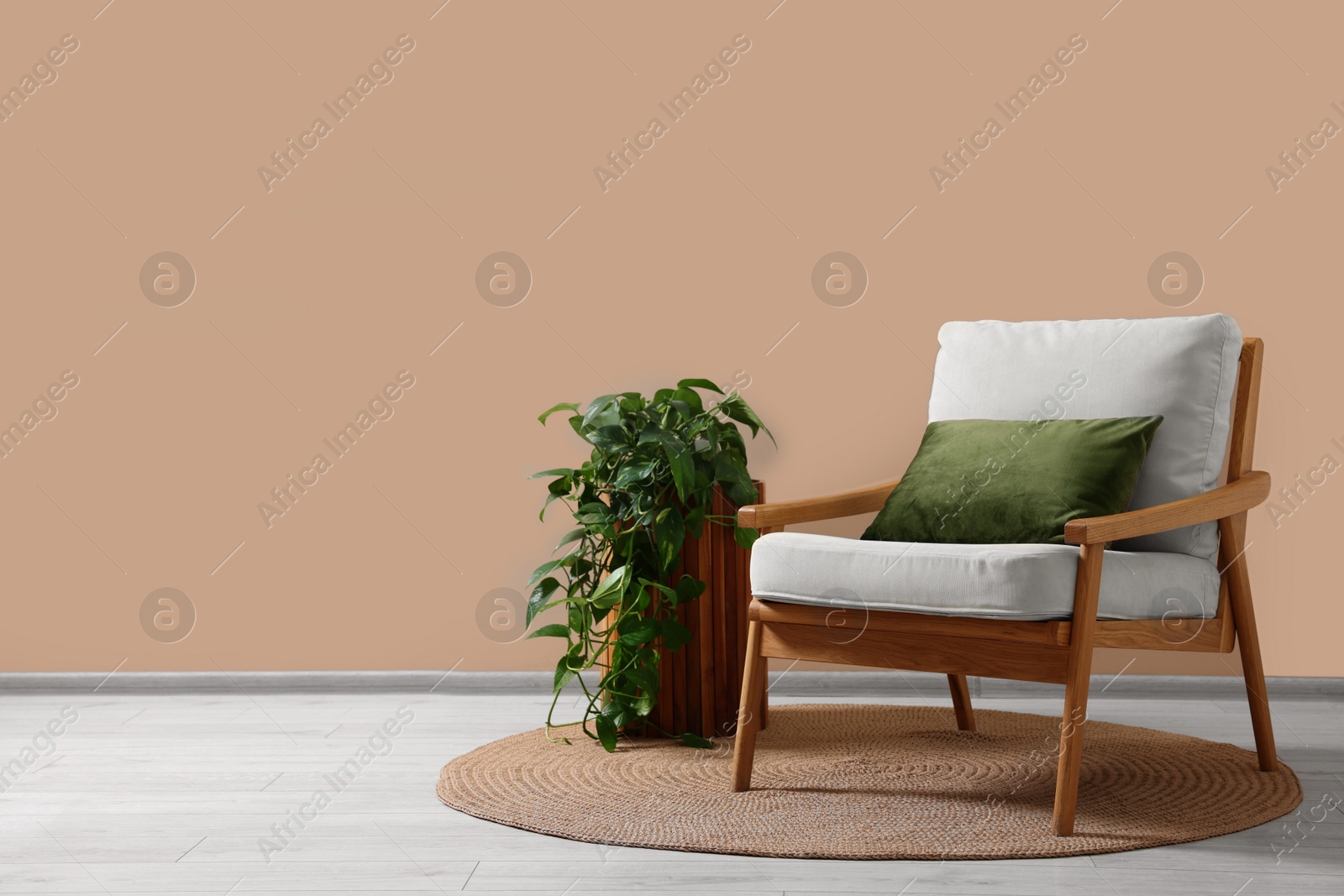 Photo of Stylish armchair with cushion and green plant near beige wall indoors, space for text