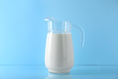 Photo of Jug of fresh milk on light blue background