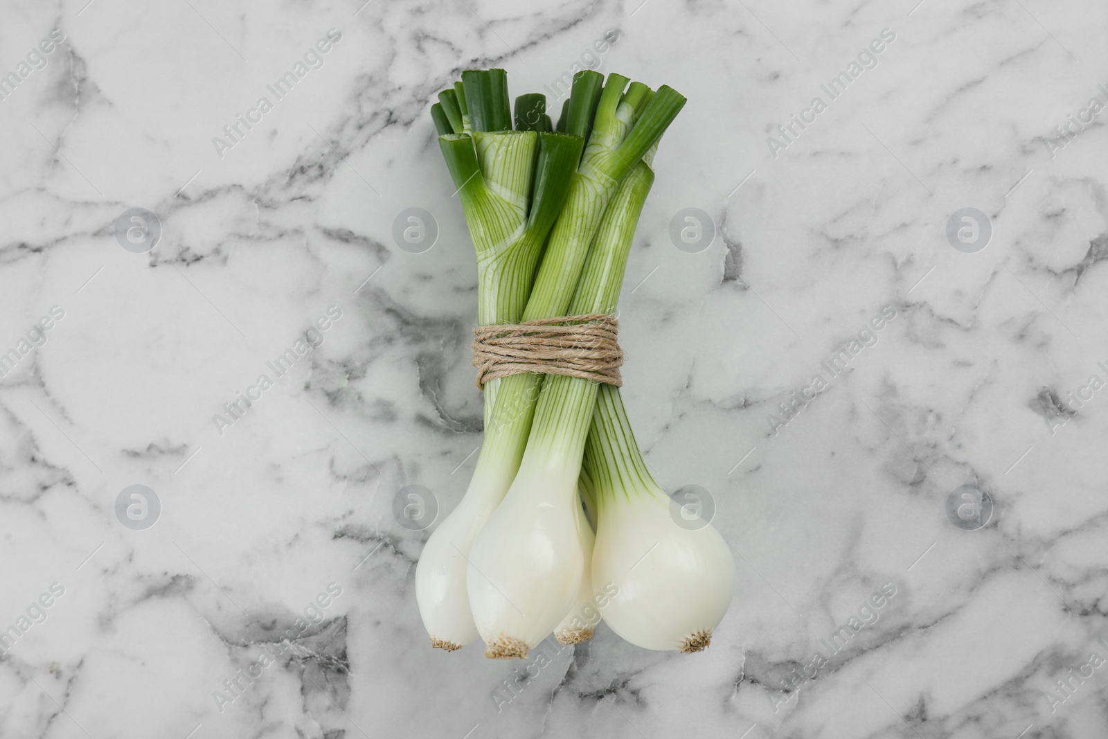 Photo of Bunch of green spring onions on white marble table, flat lay