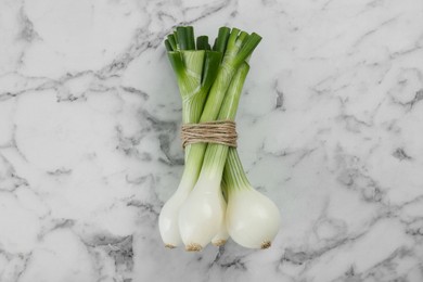 Photo of Bunch of green spring onions on white marble table, flat lay