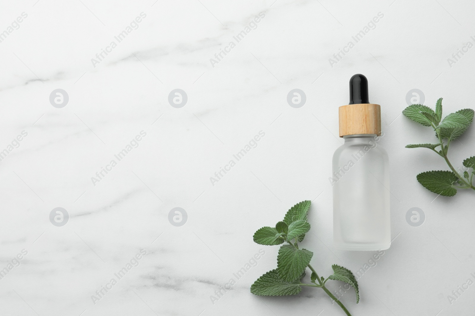 Photo of Bottle of mint essential oil and fresh herb on white marble table, flat lay. Space for text