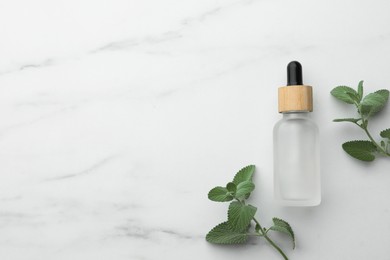 Bottle of mint essential oil and fresh herb on white marble table, flat lay. Space for text