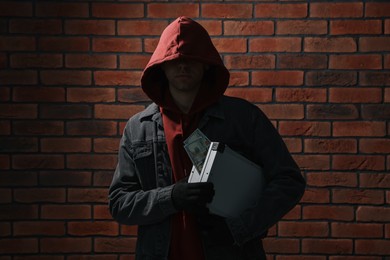 Thief in hoodie with briefcase of money against red brick wall