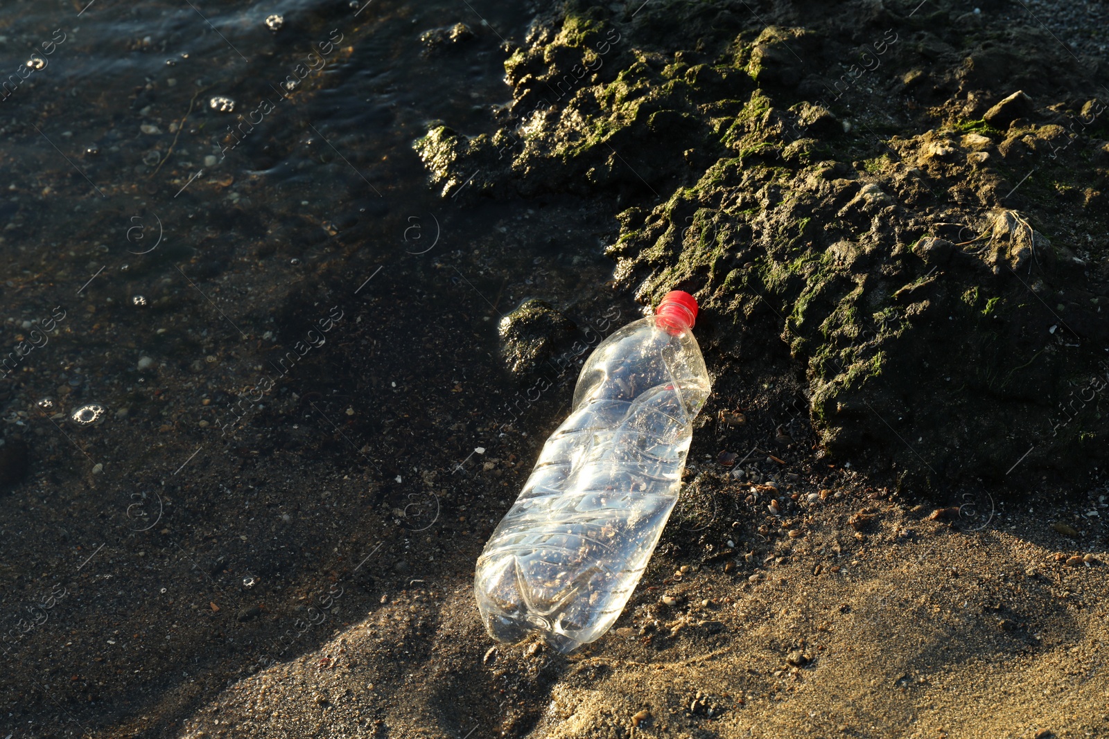 Photo of Used plastic bottle near water at beach, top view and space for text. Environment pollution