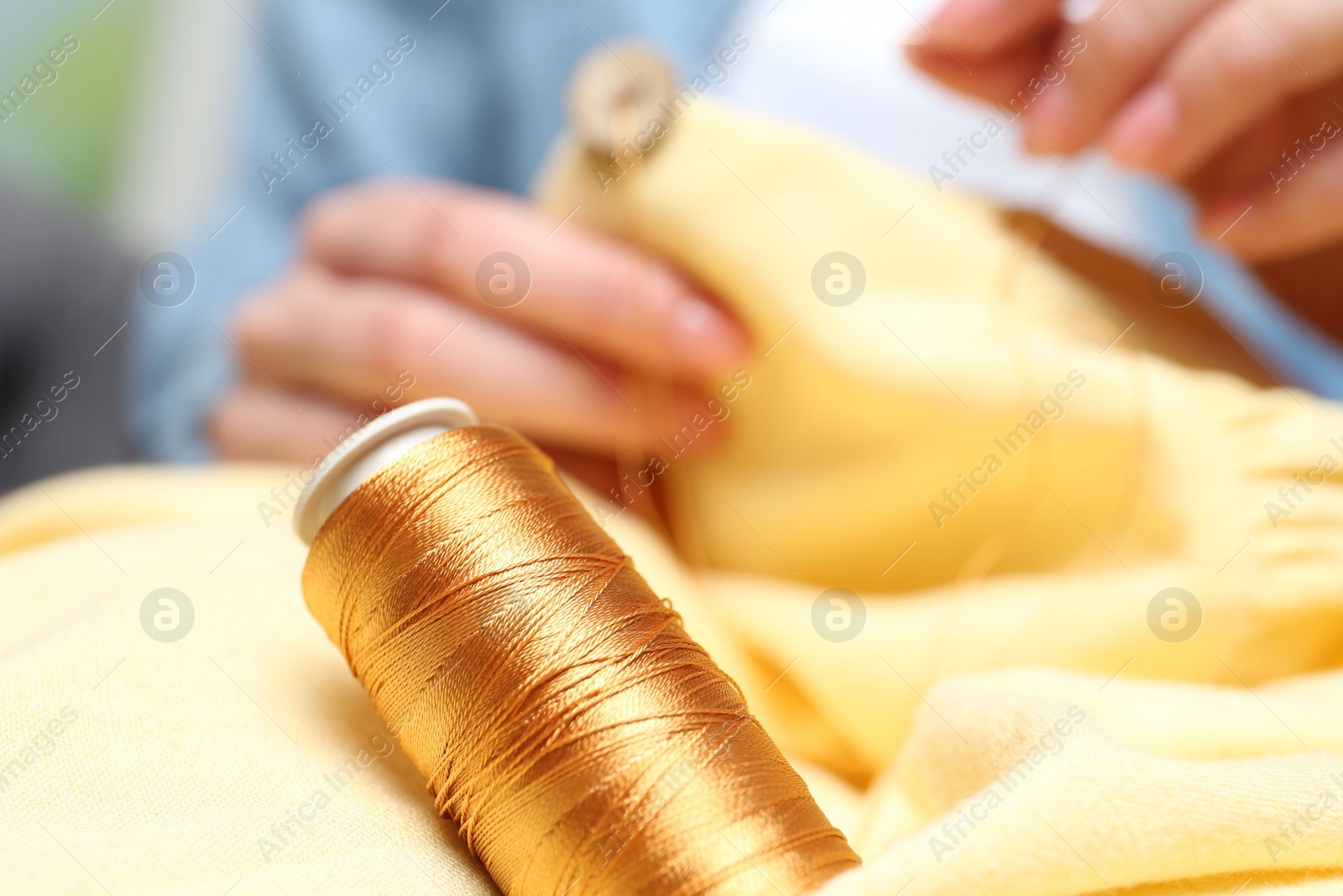 Photo of Woman sewing button onto shirt, focus on thread spool