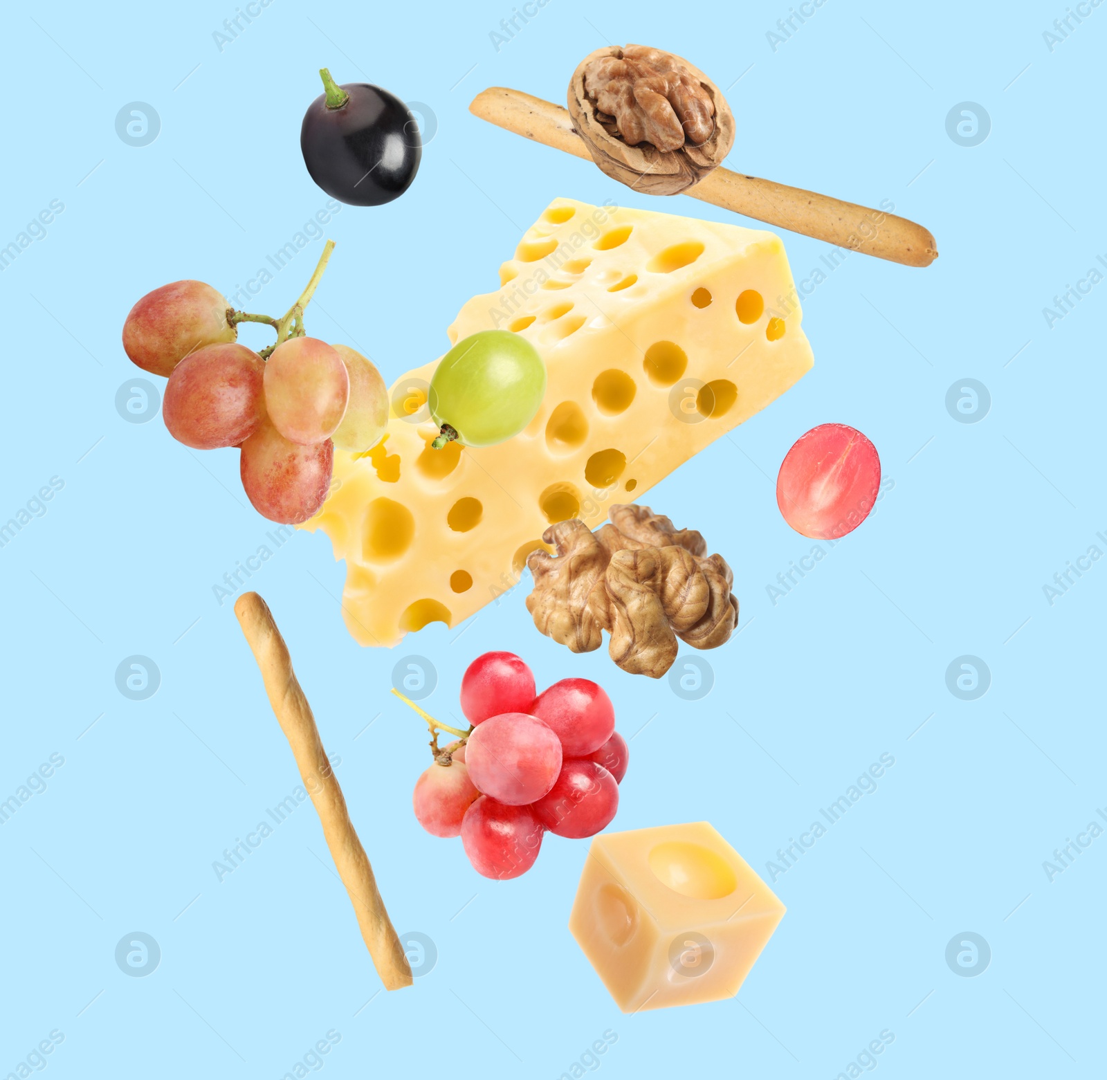 Image of Cheese, breadsticks, grapes and walnuts falling against pale light blue background