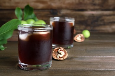 Photo of Delicious liqueur with ice and fresh walnuts on wooden table. Space for text