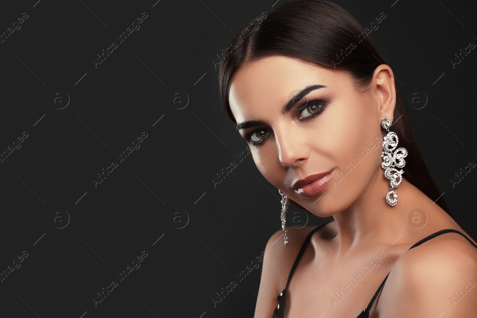 Photo of Beautiful young woman with elegant jewelry on dark background. Space for text