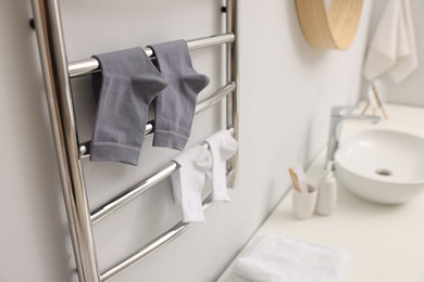 Photo of Heated towel rail with socks on white wall in bathroom