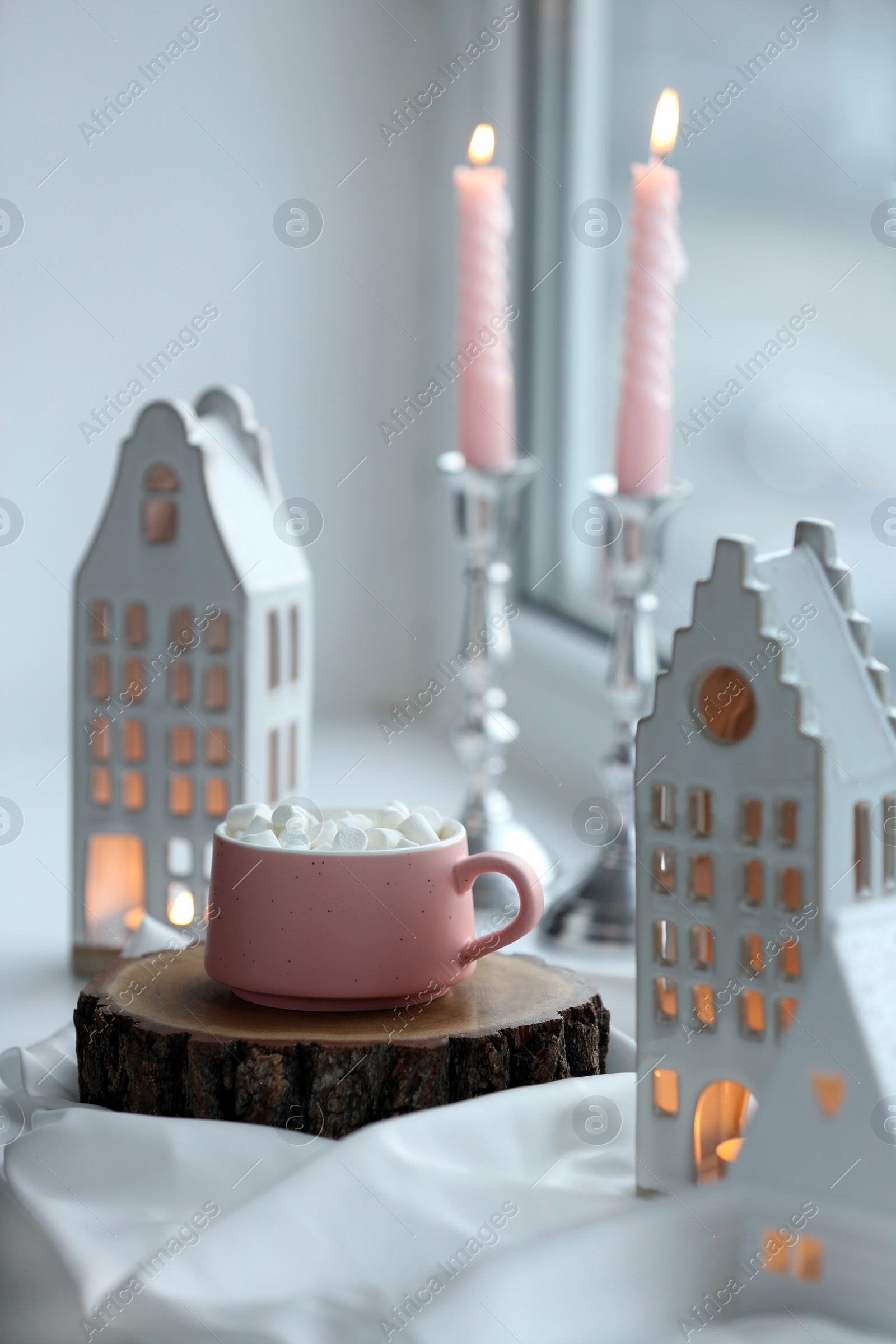 Photo of Beautiful house shaped candle holders and hot dink with marshmallow on windowsill indoors