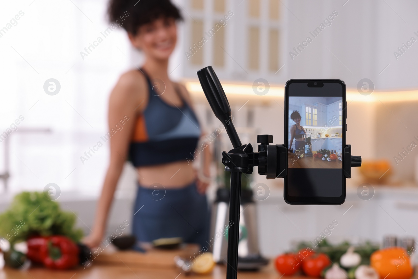 Photo of Food blogger recording video in kitchen, focus on smartphone