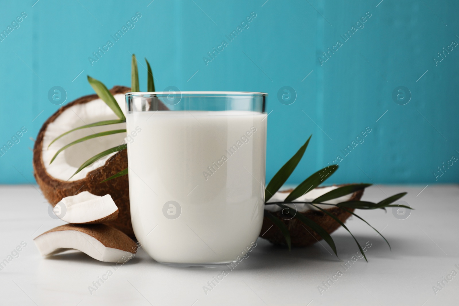 Photo of Glass of delicious vegan milk, coconut pieces and palm leaves on white marble table