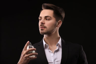 Photo of Handsome man in suit using perfume on black background