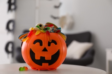 Photo of Halloween trick or treat bucket with different sweets on white table indoors