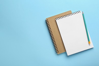 Photo of Notebooks and pencil on light blue background, top view. Space for text