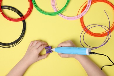 Photo of Boy drawing with stylish 3D pen on yellow background, top view