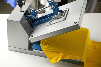 Photo of Printing logo. Heat press with yellow t-shirt on white table