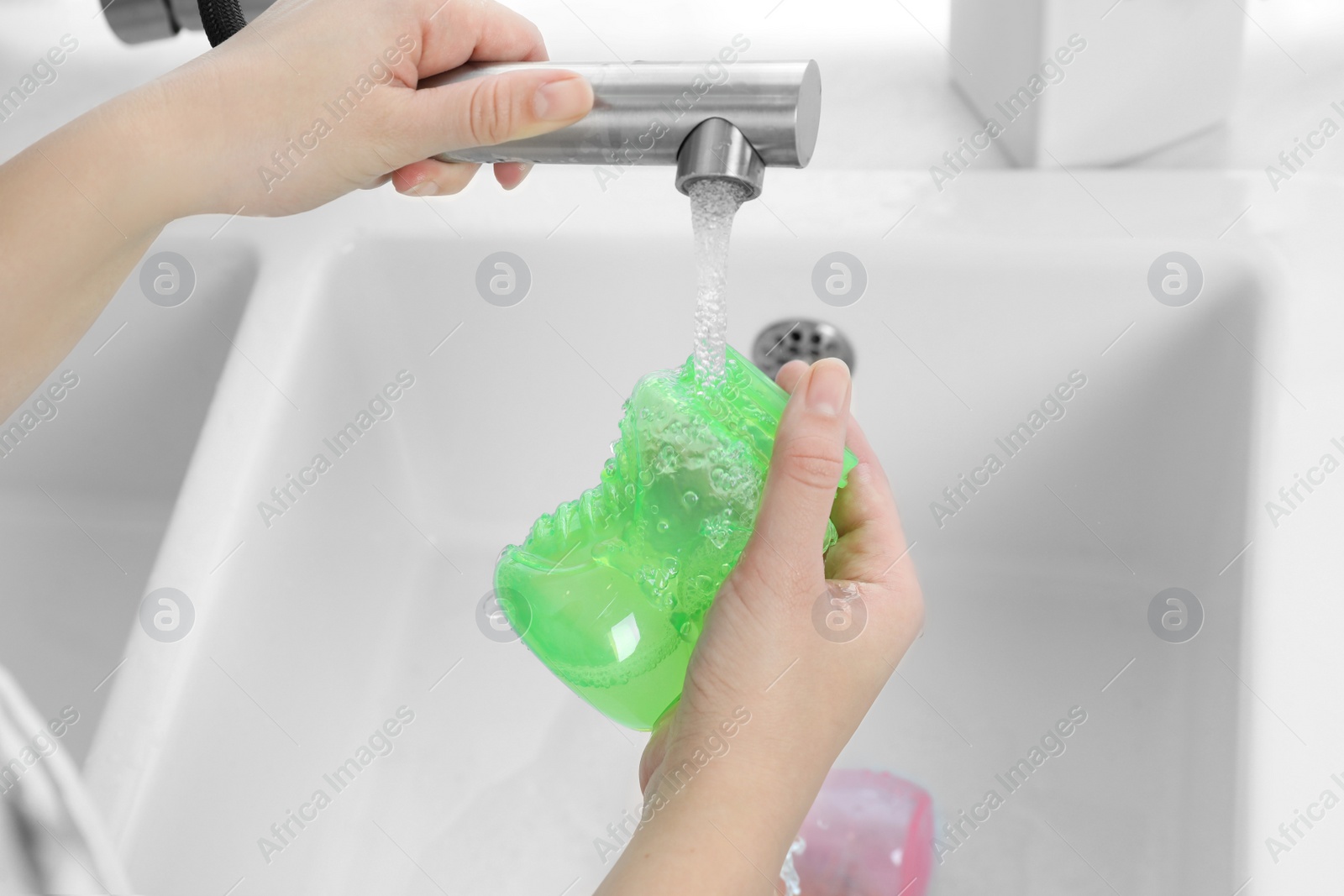 Photo of Woman washing baby bottle under stream of water in kitchen, closeup