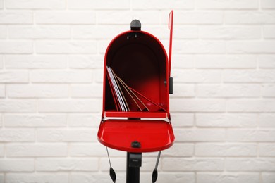 Photo of Open red letter box with envelopes near white brick wall