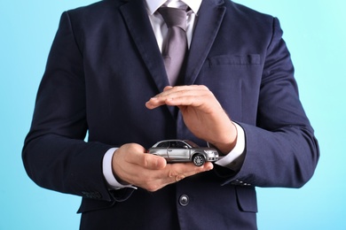 Male insurance agent holding toy car on color background, closeup