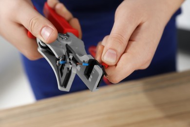 Photo of Professional electrician stripping wiring at table, closeup