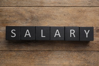 Image of Word Salary made with black cubes on wooden table, flat lay