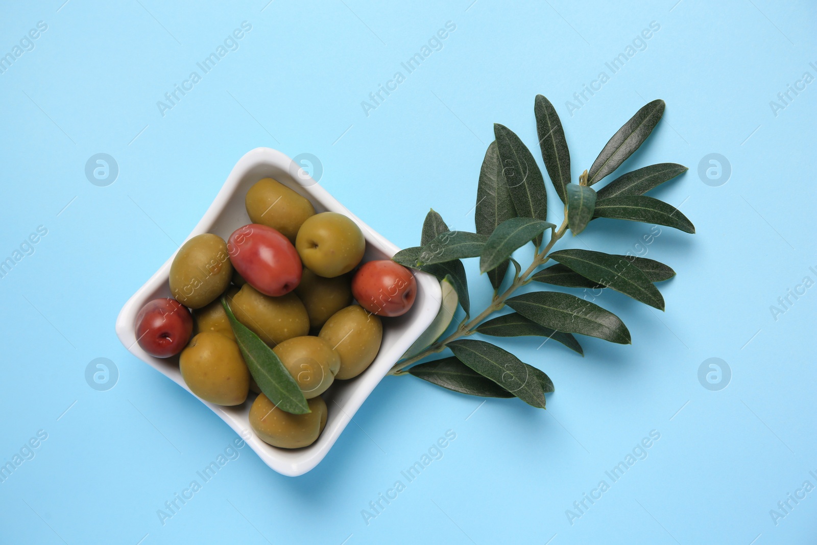 Photo of Different fresh olives and green leaves on light blue background, flat lay