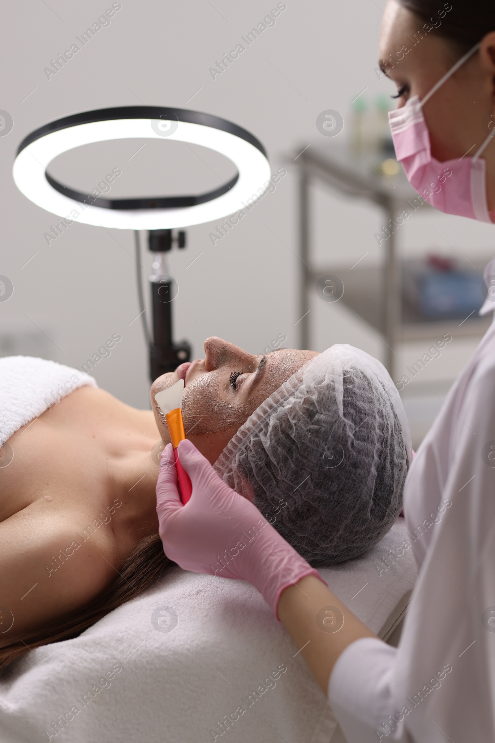 Photo of Cosmetologist applying mask on woman's face in clinic, closeup