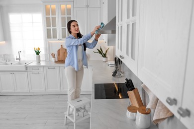 Woman on ladder wiping kitchen hood at home