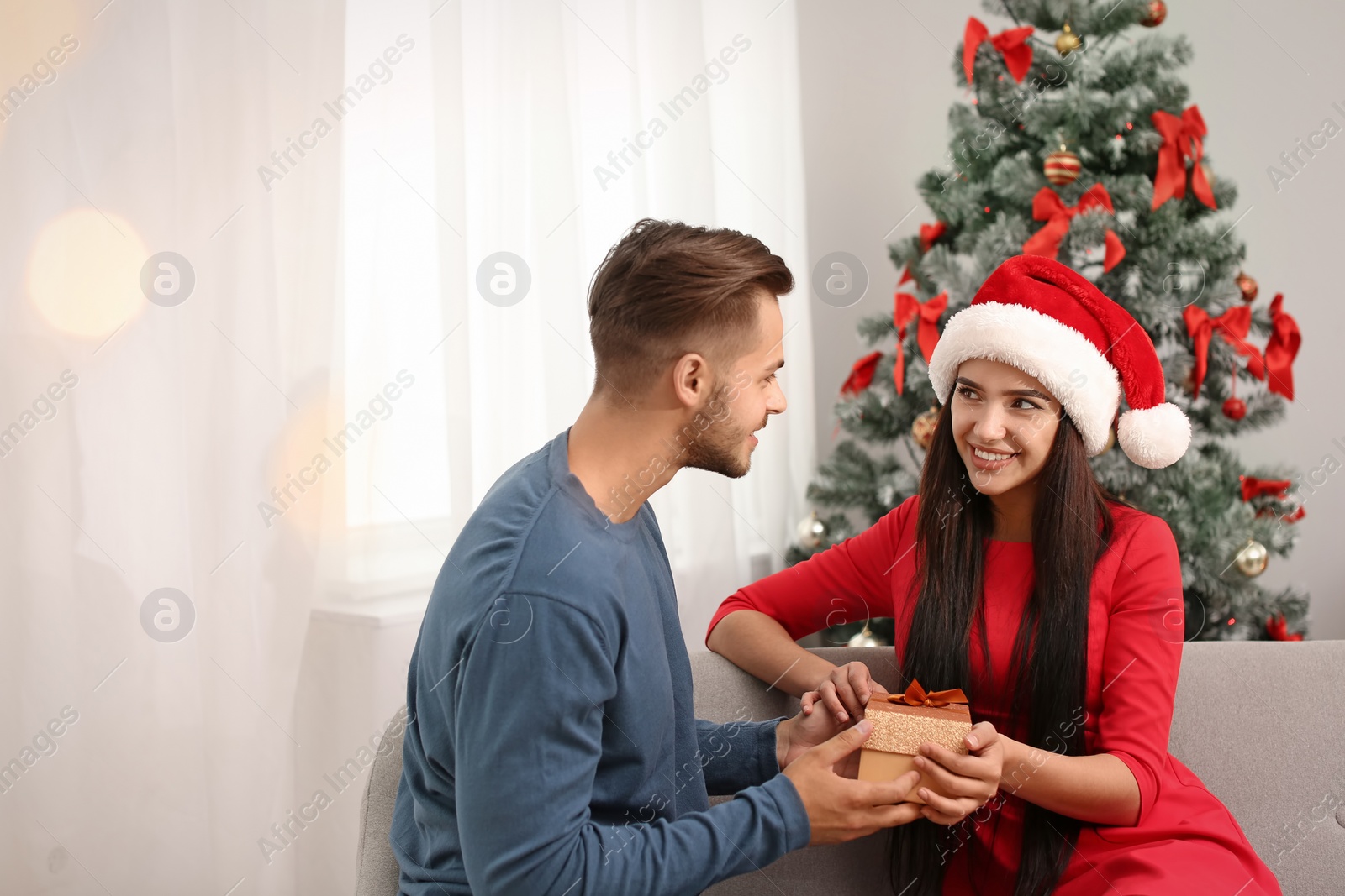 Photo of Young man giving gift box to woman at home. Happy couple celebrating Christmas