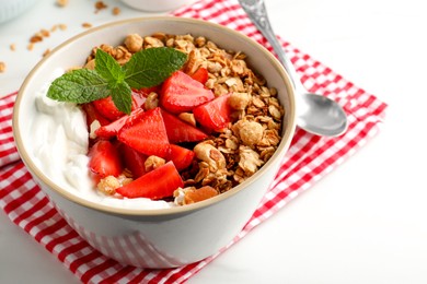 Photo of Bowl with tasty granola and strawberries served on white table, closeup. Healthy meal