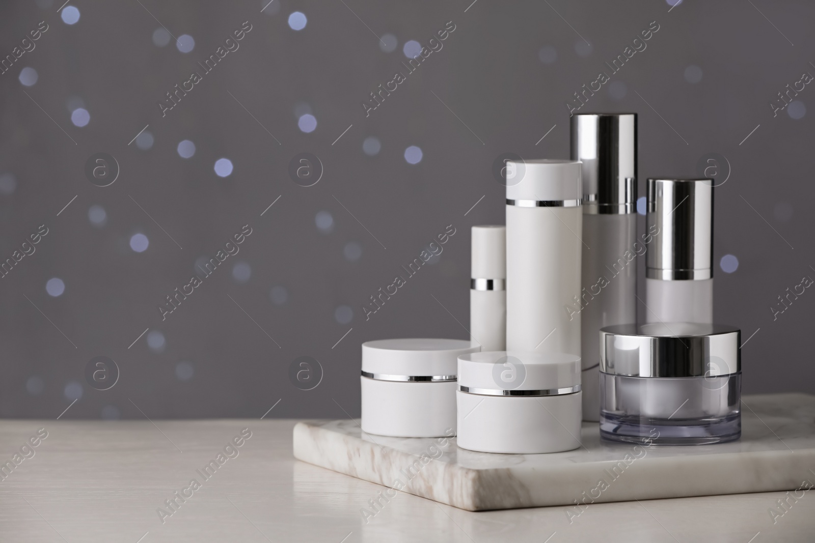 Photo of Set of skin care products on white table against blurred lights, space for text