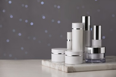 Photo of Set of skin care products on white table against blurred lights, space for text