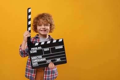 Photo of Smiling cute boy with clapperboard on orange background, space for text. Little actor