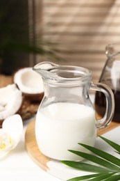 Glass jug of delicious coconut milk on white table indoors