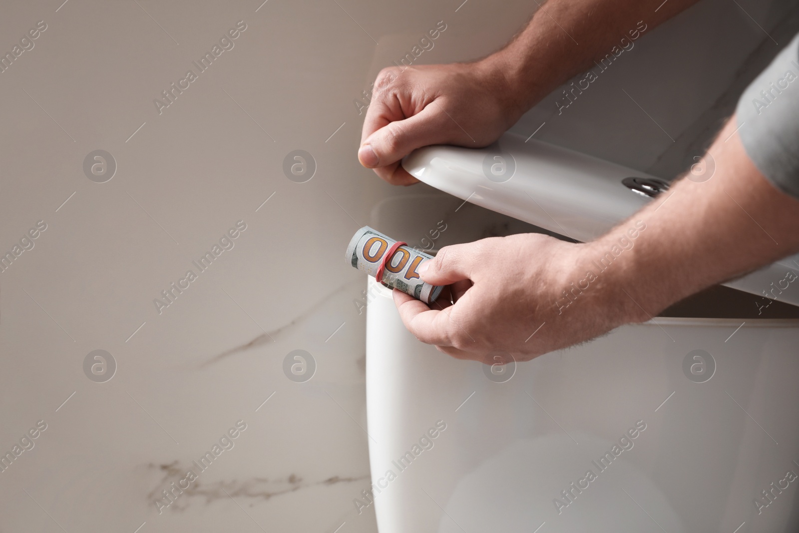 Photo of Man hiding money in toilet tank indoors, closeup. Financial savings