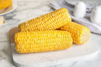 Photo of Delicious boiled corn with salt on white marble table