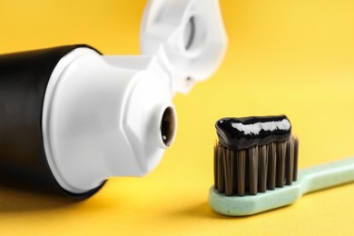 Photo of Brush and tube with charcoal toothpaste on yellow background, closeup