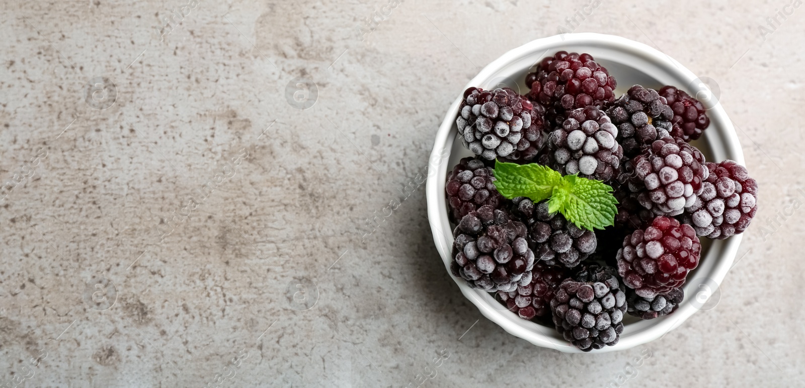 Photo of Tasty frozen blackberries with mint on grey table, top view. Space for text