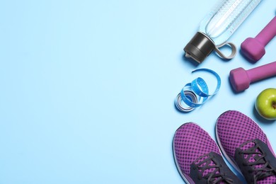 Flat lay composition with sneakers and dumbbells on light blue background. Space for text