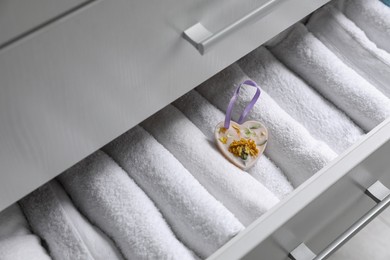 Photo of Beautiful heart shaped scented wax sachet in dresser drawer with white towels, closeup