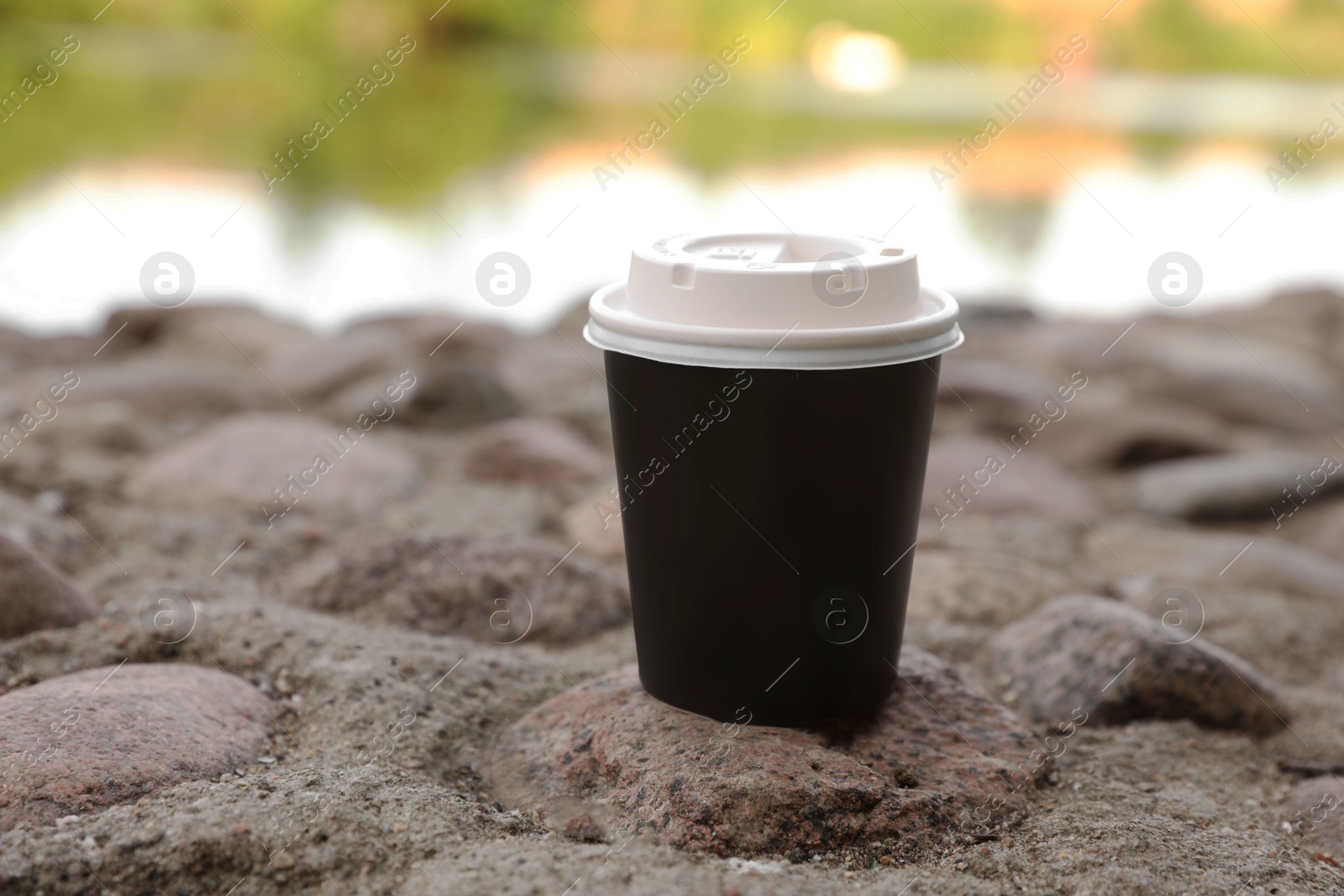 Photo of Paper cup on rocky ground outdoors, closeup. Coffee to go