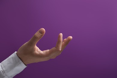 Photo of Man holding something in hand on purple background, closeup. Space for text
